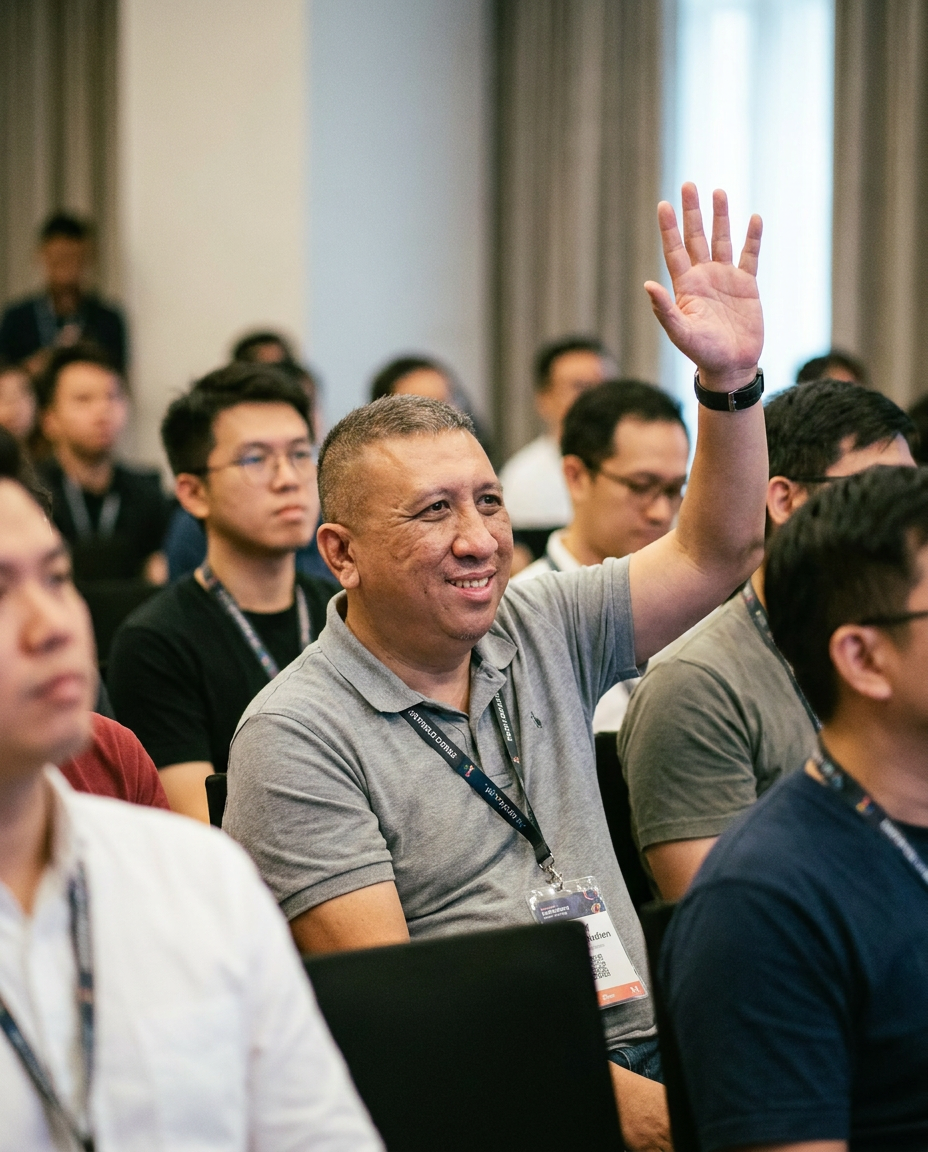 Conference Q&A participant portrait with hand raised to ask a question.